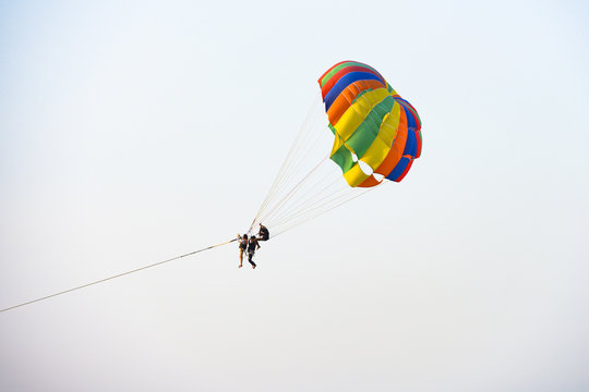 Three unidentified tourists do parasailing during sunset in Patong beach, Phuket, Thailand. Parasailing is a recreational kiting activity where a person is towed behind a vehicle (usually a boat).