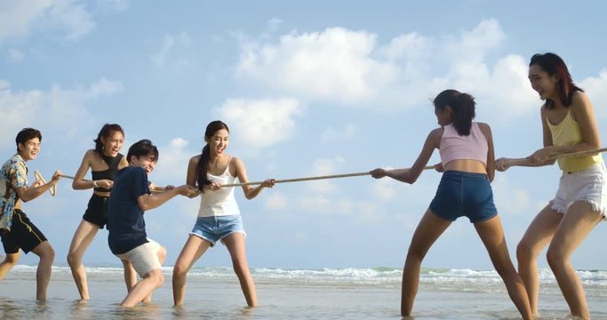 Group of Young People Having Fun on the Beach. Smiling friends playing tug of war at beach on a sunny day. People with party celebration concept. 4K resolution. Slow motion shot.