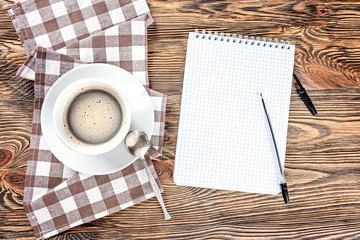 A cup of black hot coffee and notepad on a wooden table.