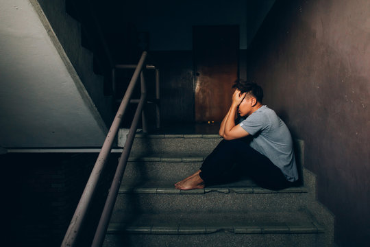 Depressed man sitting on the stairs in building and holding his forehead while having headache.Depression concept.Effect from coronavirus