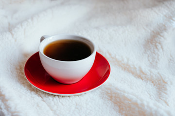 Big white morning cup of coffee and red plate in bed with pillow and cosy blanket.