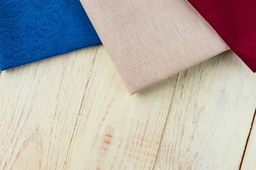 Top view of cloth napkins of beige, blue and burgundy colors on rustic white background.
