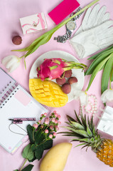 Women's accessories in white and pink colors whith tropical fruits. Mango, pineapple, pitahaya, lychee flowers, notebook with pen, cosmetics and gift boxes. Beauty women flat lay. Top view.