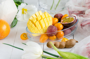 Exotic fruits and flowers on white wooden background.