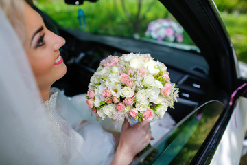 Blonde beautiful bride posing in car with bouquet of flowers in hands