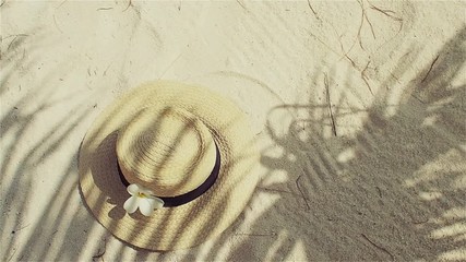 Straw hat on sand, sun protection concept. Still life with a hat and shades of palm leaves