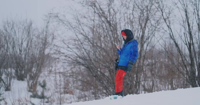 Slow motion shot of a snowboarder using a smartphone while driving on a ski slope