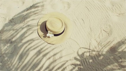 Straw hat on sand, sun protection concept. Still life with a hat and shades of palm leaves