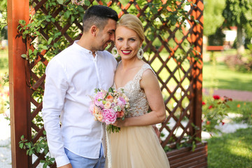 Beautiful blonde bride with groom holding bouquet of flowes at park