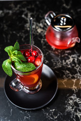 fruit tea with cranberries, teapot and glass, dark background