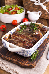 Grilled pork ribs. Meat with spices and herbs in dishes on wooden background. Lunch barbecue with salad and sauce. Free space for the text