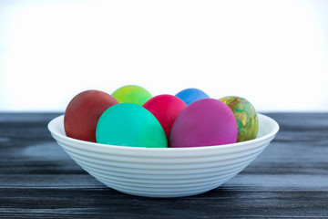White plate of Easter multicolored boiled eggs on black wood
