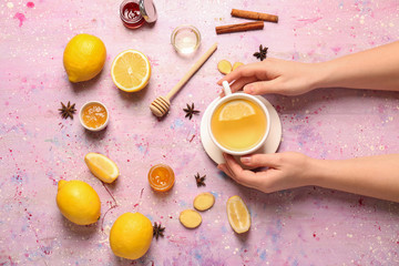 Female hands with cup of tasty tea, lemon and ginger on color background