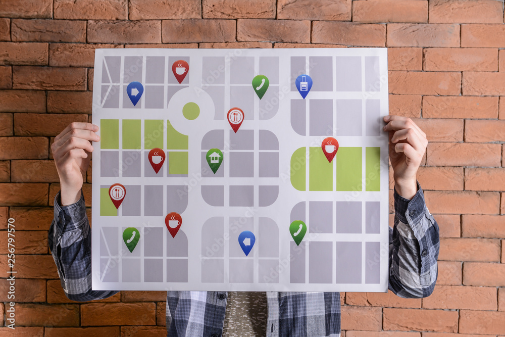 Wall mural man holding map of city with location pointers near brick wall