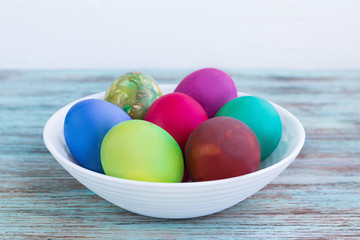 White plate of Easter versicolored boiled eggs on wooden background