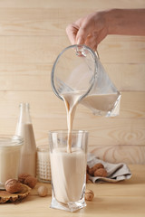 Woman pouring tasty vegan milk from jug into glass on wooden background