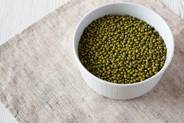 Raw green mung beans in a gray bowl over white wooden surface, low angle view.