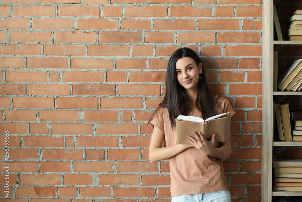 Wall mural Beautiful young woman with book near brick wall in library