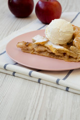 Slice of home-baked apple pie with ice cream on pink plate, low angle view. Closeup.
