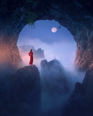 Woman in red dress against the moon in spooky cave