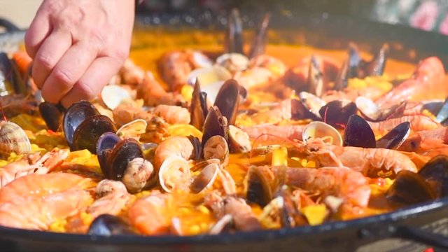 Paella. Person cooking traditional spanish seafood paella with prawns, mussels and fish closeup. Slow motion 4K UHD video footage. 3840X2160