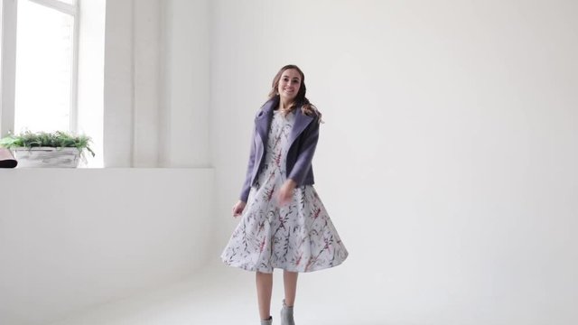 Beautiful girl walking in a coat on a white background, smiling and having fun, slow motion