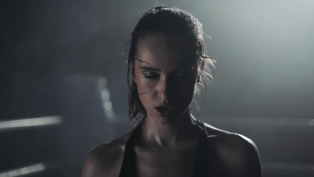 Portrait of tired female boxer standing on the boxing ring and looking intensely at the camera
