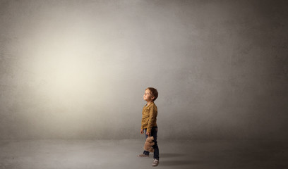 Little waggish kid staying alone in a big empty room with his plush
