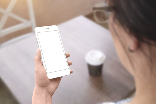 Woman hold white smart phone with isolated screen for mockup. Coffee shop table in background.