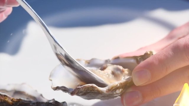 Oysters on ice with lemon closeup. Person eating fresh oyster on half shell on big plate in restaurant. Slow motion 4K UHD video footage. 3840X2160