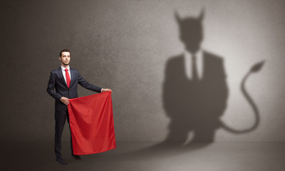 Businessman standing with red cloth in his hand and devil shadow on the background
