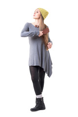  Young stylish woman with beanie cap brushing long blonde hair with hairbrush. Full body isolated on white background. 