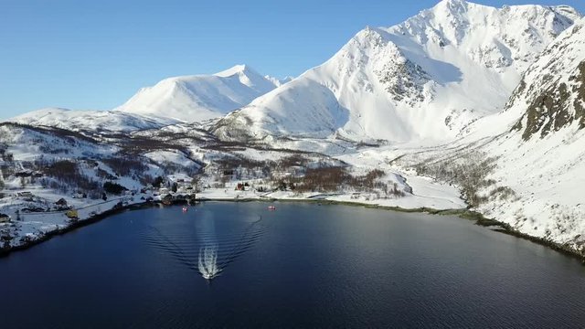 aerial tracking shot,rubber boat sailing in winter open water brash ice .daylight clear blue sky,the sun is shining so bright on the entire snow covered mountains and trees. norway getaway in 4K 30fps
