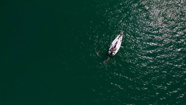 people in the middle of the sea swimming around a sailboat
