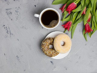 Two donuts and coffee cup with tulips. Gray background, top view, space for text
