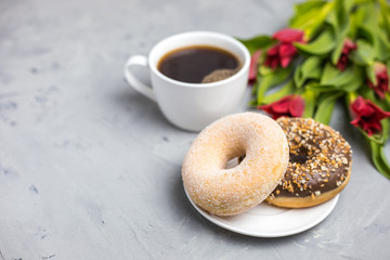 Two donuts and coffee cup with tulips. Gray background, top view, space for text