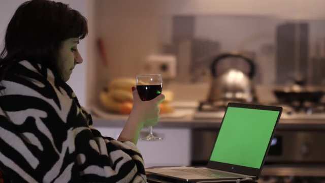 woman sits with a glass of wine in the evening at home and looks at a laptop, chroma key