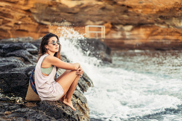 Pretty long hair brunette tourist girl relaxing on the stones near sea.