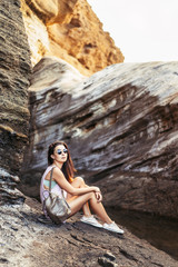 Pretty long hair brunette tourist girl relaxing on the stones near sea.