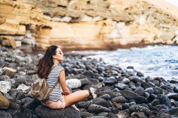 Pretty long hair tourist girl relaxing on the stones near sea.