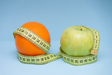 Orange and apple with measuring tape wrapped around them on the blue background.