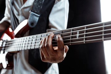 African American handsome jazz musician playing bass guitar in the studio on a black background. Music concept. Young joyful attractive guy improvising. Close-up retro portrait.