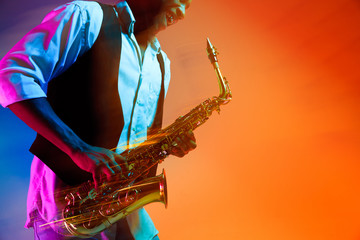 African American handsome jazz musician playing the saxophone in the studio on a neon background....