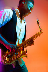 African American handsome jazz musician playing the saxophone in the studio on a neon background....