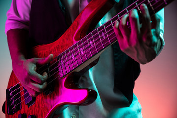 African American handsome jazz musician playing bass guitar in the studio on a neon background. Music concept. Young joyful attractive guy improvising. Close-up retro portrait. - obrazy, fototapety, plakaty