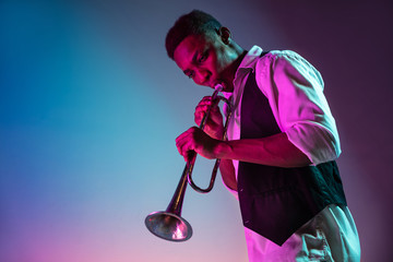 African American handsome jazz musician playing trumpet in the studio on a neon background. Music...
