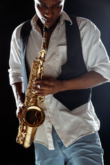 African American handsome jazz musician playing the saxophone in the studio on a black background....