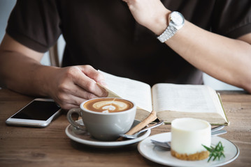 Relax Asian man drink coffee and read book in a modern style coffee shop - people with coffee cup easy lifestyle concept