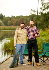 leisure and people concept - happy friends with fishing rods and scoop net at lake or river