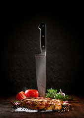 Beef steak on a wood desk with chef knife. Around are fresh tomatoes, sweet and spicy peppers,...